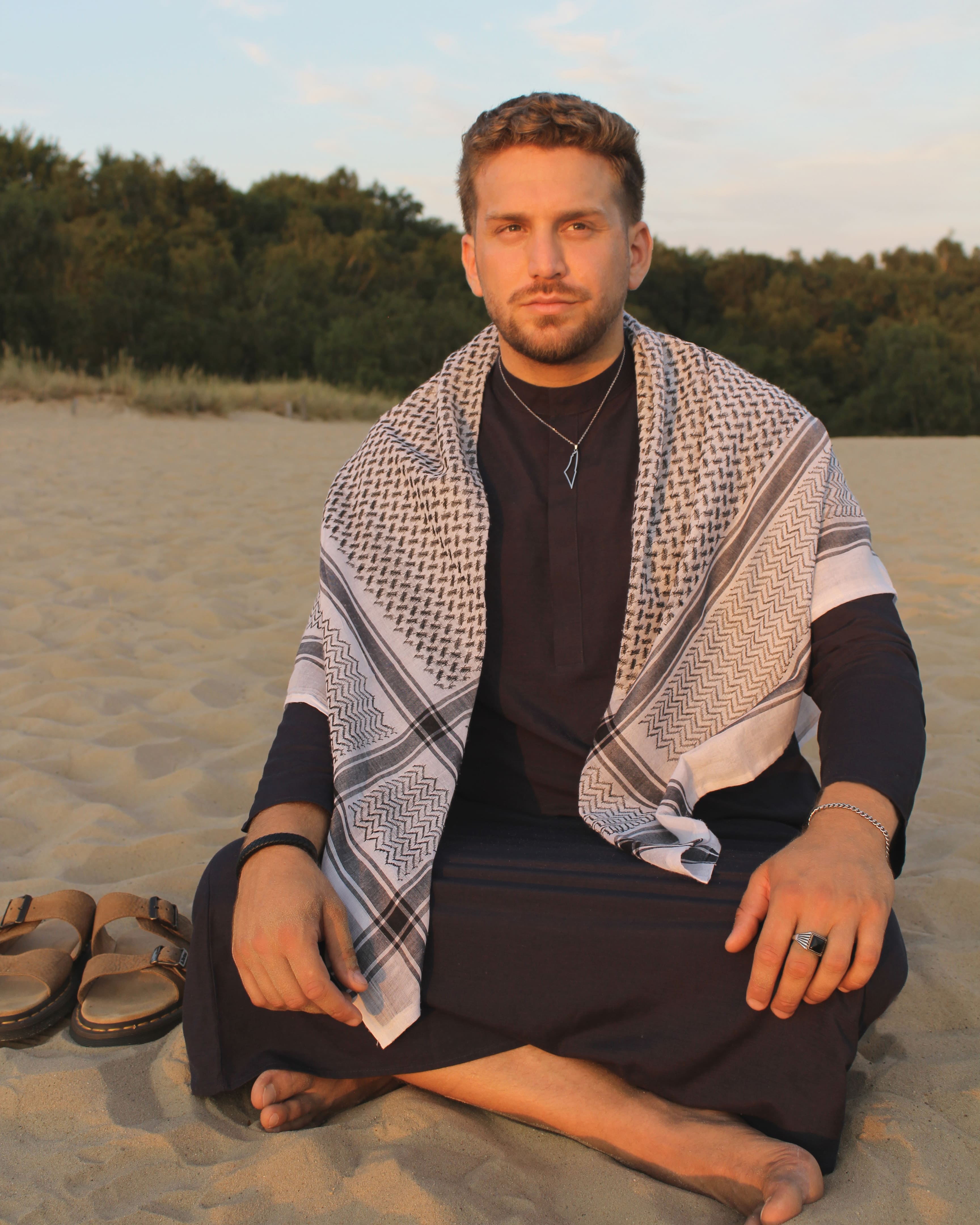 Mann im dunkelblauen Ocean Thobe sitzt entspannt im Freien – moderne islamische Kleidung für Herren
